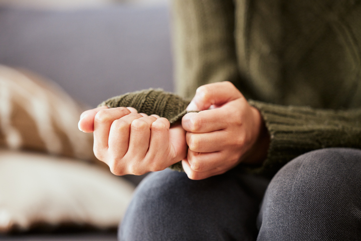 A woman sitting on a sofa, anxiously tugging the sleeve of her sweater, representing the feelings of worry and unease that counselling can help with.