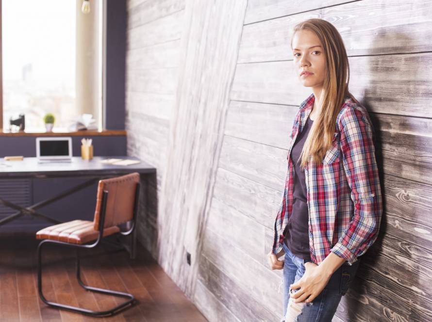 slim young woman casually dressed in jeans and a checked shirt, standing with arms crossed in an office – representing body image counselling and self-acceptance