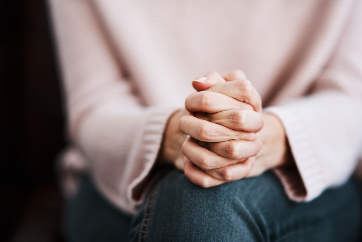 Woman sitting with hands clasped, reflecting perfectionist tendencies