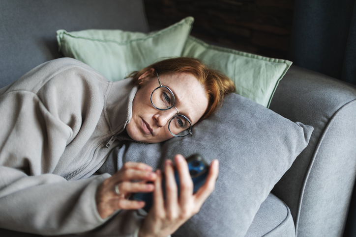Woman lying on sofa doom scrolling, feeling overwhelmed by perfectionist pressures