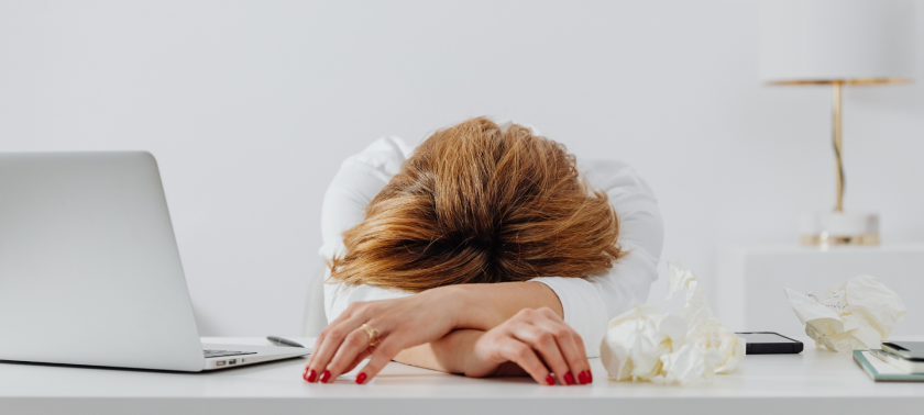 A professional woman resting her head on her desk, appearing exhausted, symbolising the emotional toll of perfectionism.