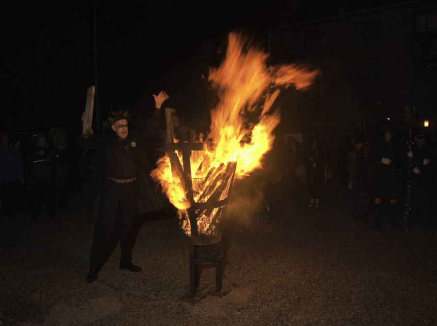 Man in pagan-style costume near a lit beacon at a winter solstice celebration