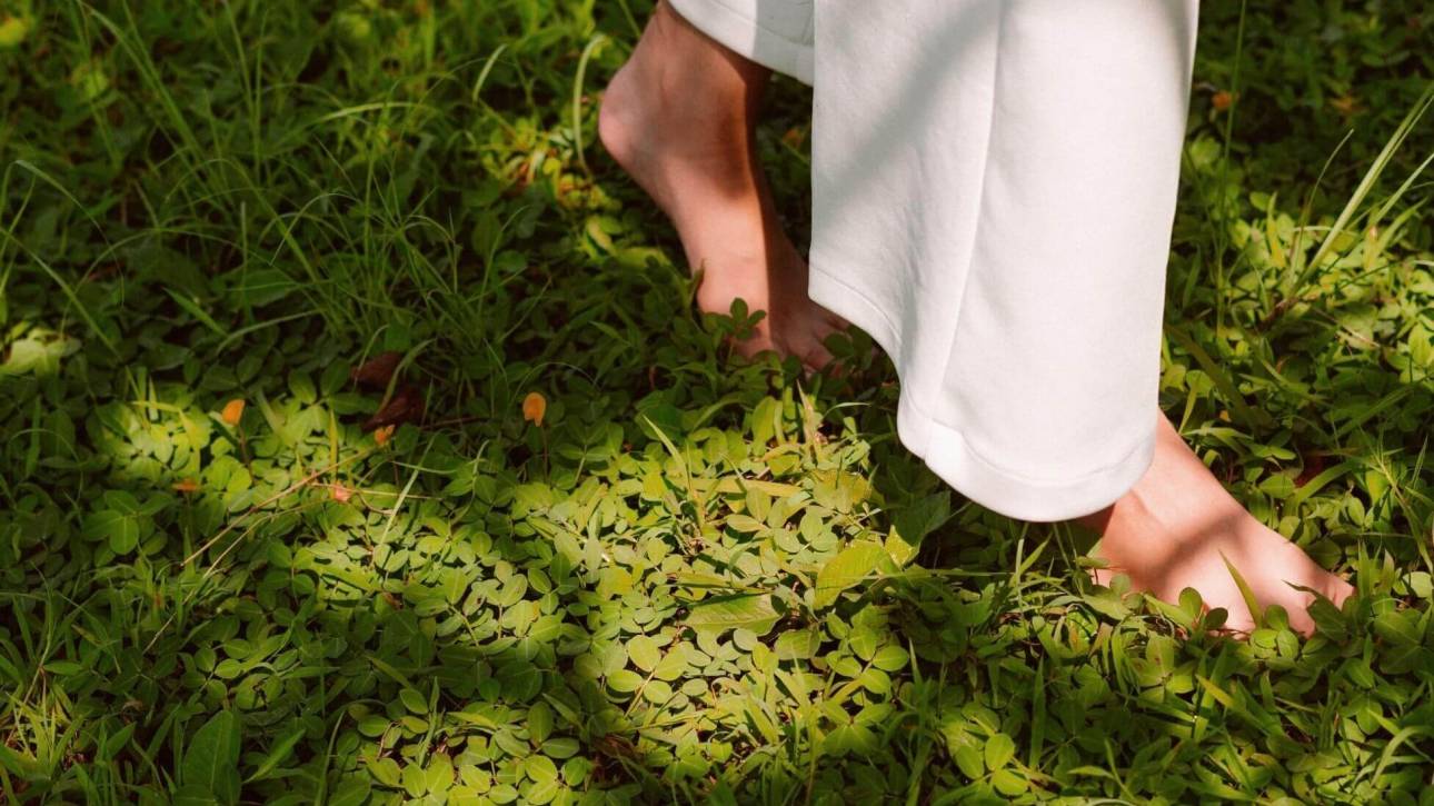 A person walking barefoot on grass, with only their lower legs visible