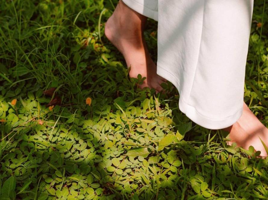 A person walking barefoot on grass, with only their lower legs visible