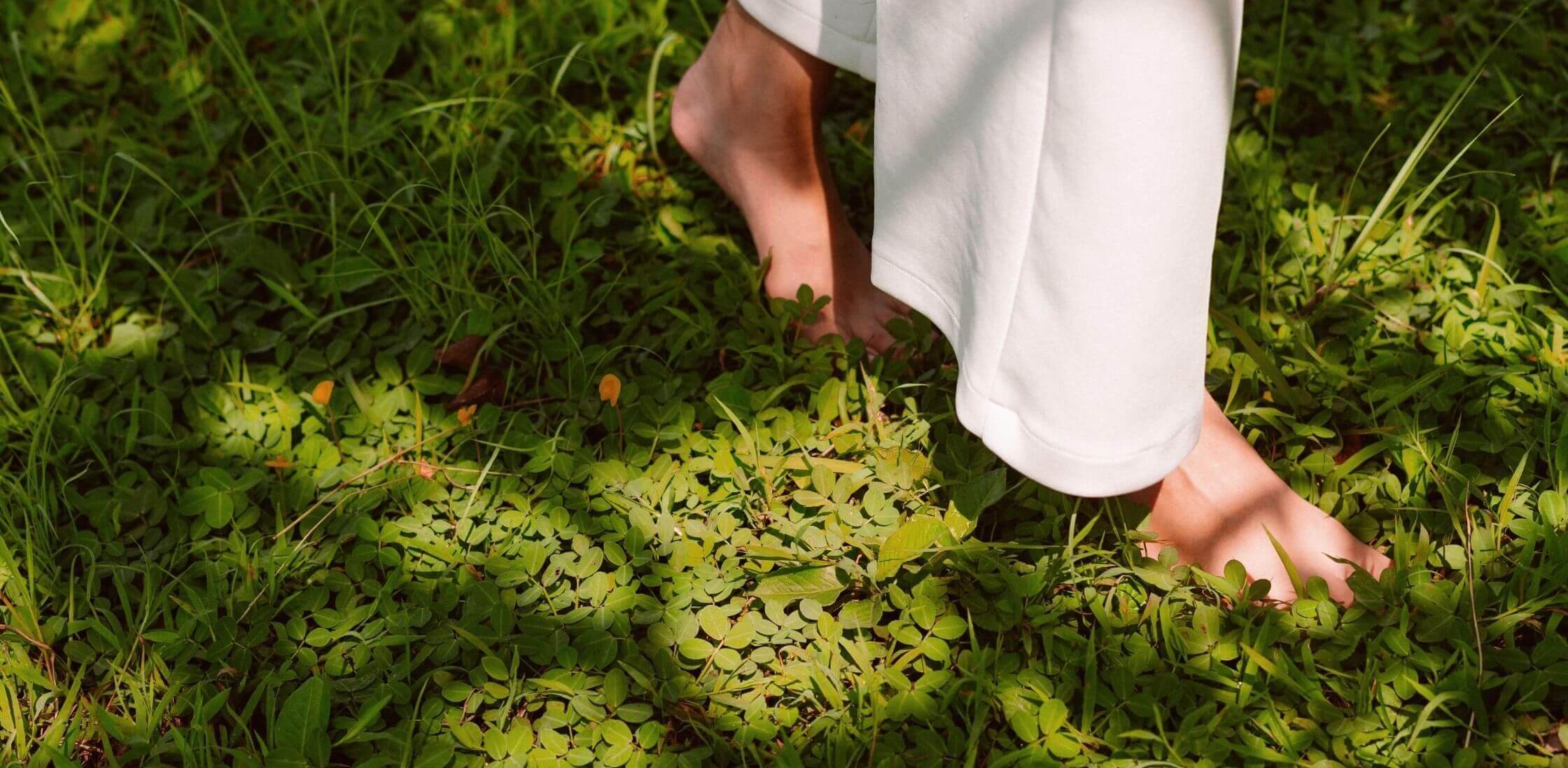 A person walking barefoot on grass, with only their lower legs visible