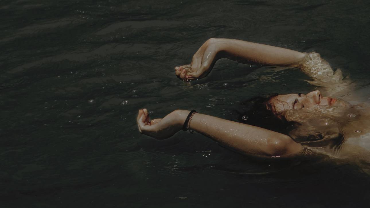 Person floating peacefully in water with arms outstretched, suggesting surrender and release, representing letting go of 'should' statements