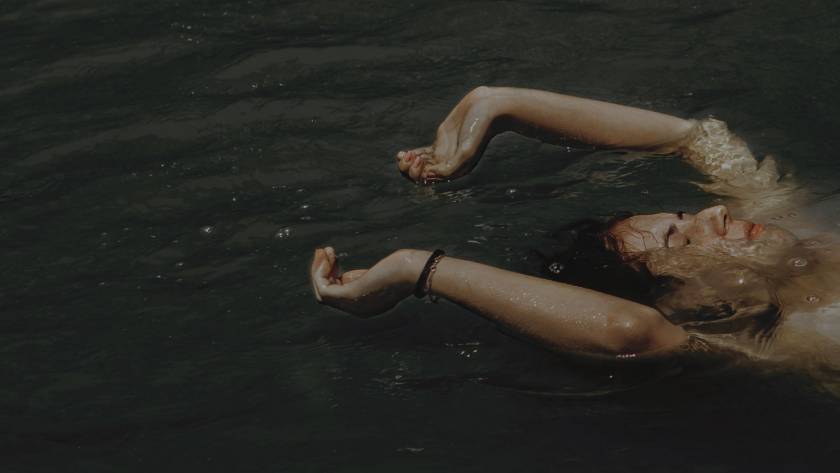 Person floating peacefully in water with arms outstretched, suggesting surrender and release, representing letting go of 'should' statements