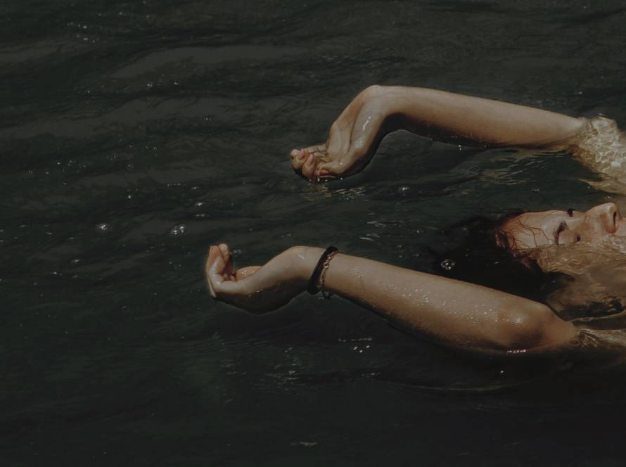 Person floating peacefully in water with arms outstretched, suggesting surrender and release, representing letting go of 'should' statements