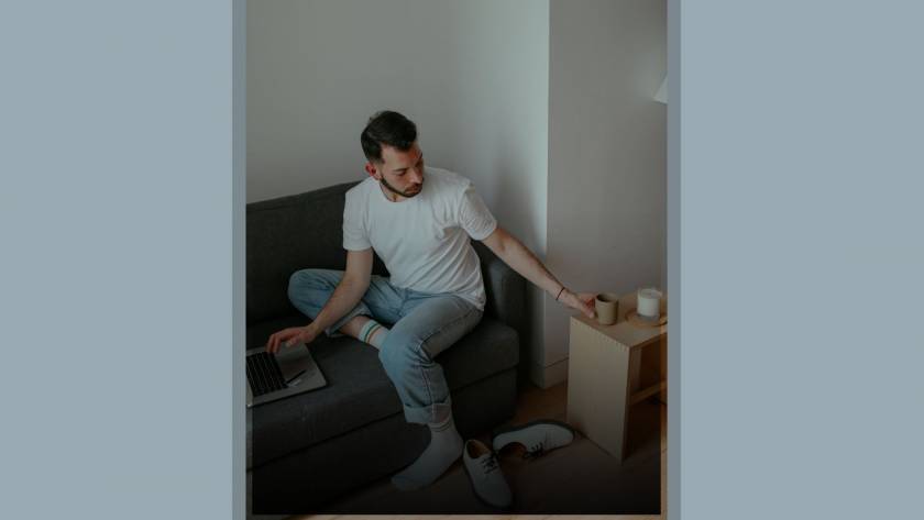 Young man in casual clothing turning away from laptop to reach for coffee, representing disconnecting from social media comparison