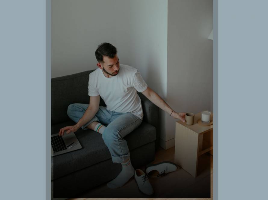 Young man in casual clothing turning away from laptop to reach for coffee, representing disconnecting from social media comparison