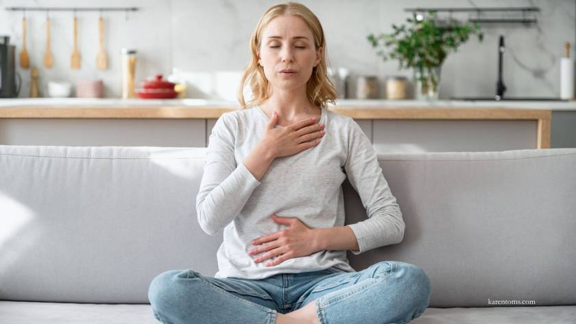 Young woman sitting peacefully on sofa with one hand on her chest and one on her stomach, demonstrating body awareness and self-connection