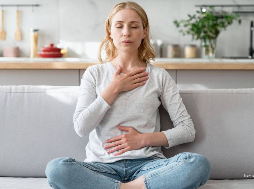 Young woman sitting peacefully on sofa with one hand on her chest and one on her stomach, demonstrating body awareness and self-connection