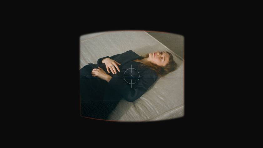 Woman in suit lying on bed looking reflective and sad, representing internal conflict with self