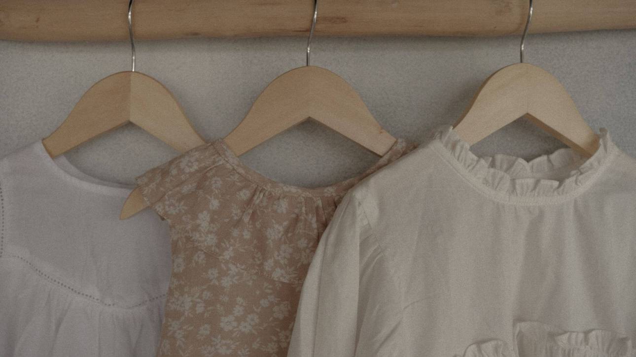 Neutral colored clothes hanging on wooden rail - spring wardrobe anxiety