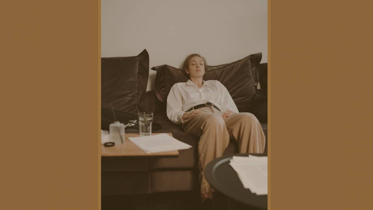 A woman resting on a dark sofa surrounded by papers — burnout vulnerability explored by Karen Toms therapist and counsellor