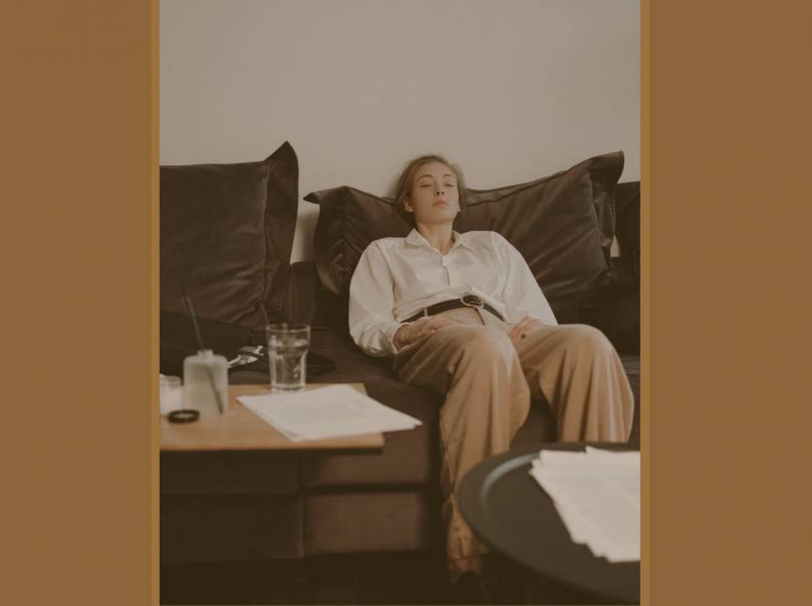 A woman resting on a dark sofa surrounded by papers — burnout vulnerability explored by Karen Toms therapist and counsellor