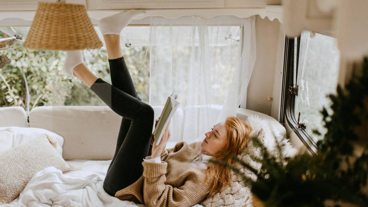 A woman lying on a bed reading a book in a bright, cosy space capturing the quiet contentment of an introvert happily in their own company