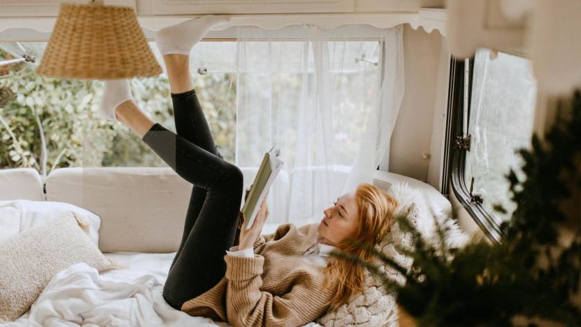 A woman lying on a bed reading a book in a bright, cosy space capturing the quiet contentment of an introvert happily in their own company