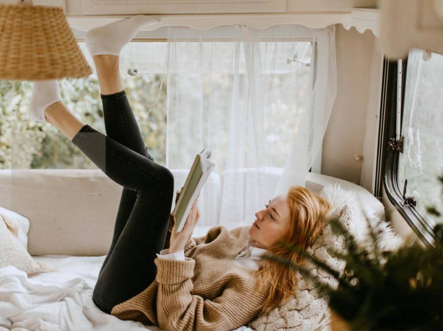 A woman lying on a bed reading a book in a bright, cosy space capturing the quiet contentment of an introvert happily in their own company