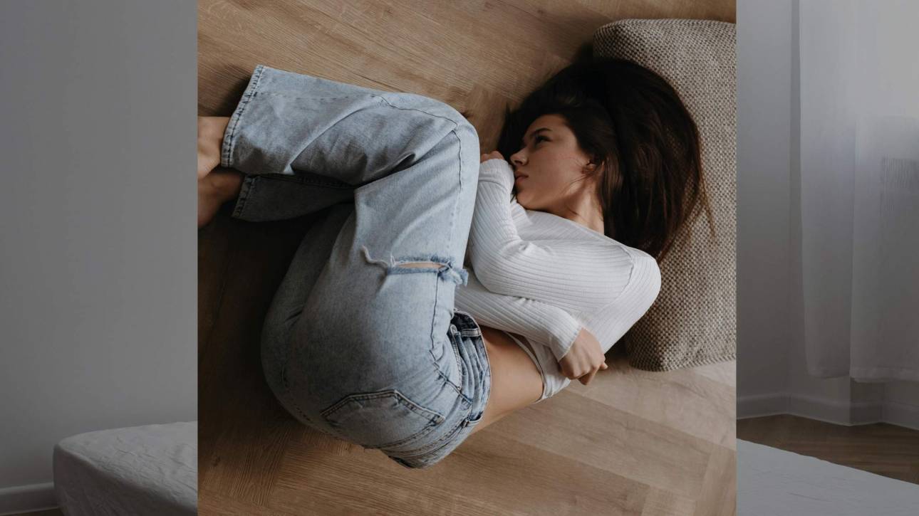 Woman lying in foetal position on a warm wooden floor, overhead angle, depicting quiet exhaustion and withdrawal