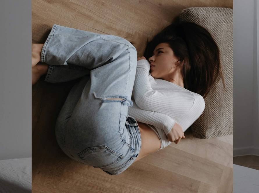 Woman lying in foetal position on a warm wooden floor, overhead angle, depicting quiet exhaustion and withdrawal