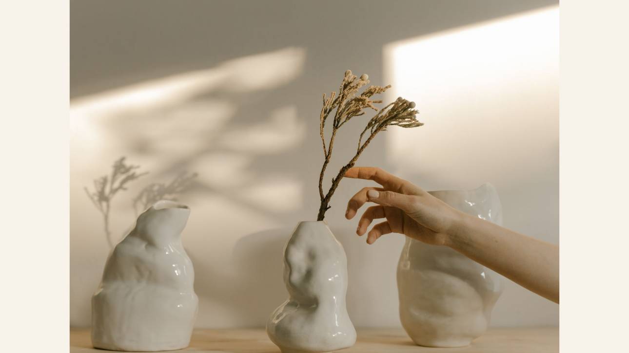 Hand reaching in to arrange imperfect white ceramic vessels in warm natural light, illustrating the fawning pattern of orchestrating and controlling