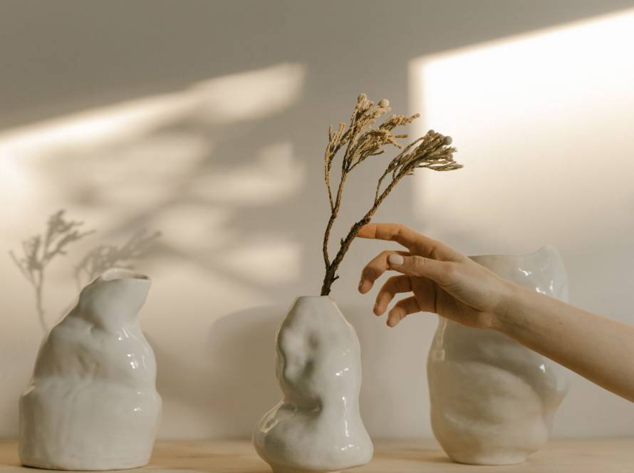 Hand reaching in to arrange imperfect white ceramic vessels in warm natural light, illustrating the fawning pattern of orchestrating and controlling