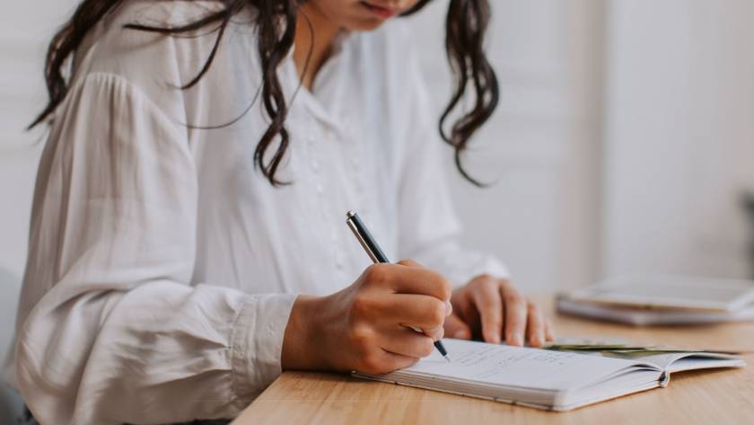 Woman writing in a journal at a desk in warm natural light, real and unposed