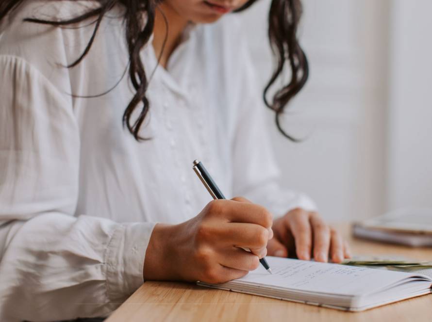 Woman writing in a journal at a desk in warm natural light, real and unposed