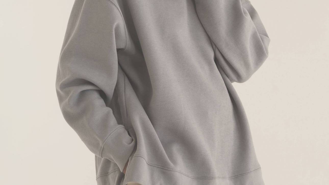 A figure in an oversized neutral sweatshirt, partially hidden, illustrating clothes as disguise