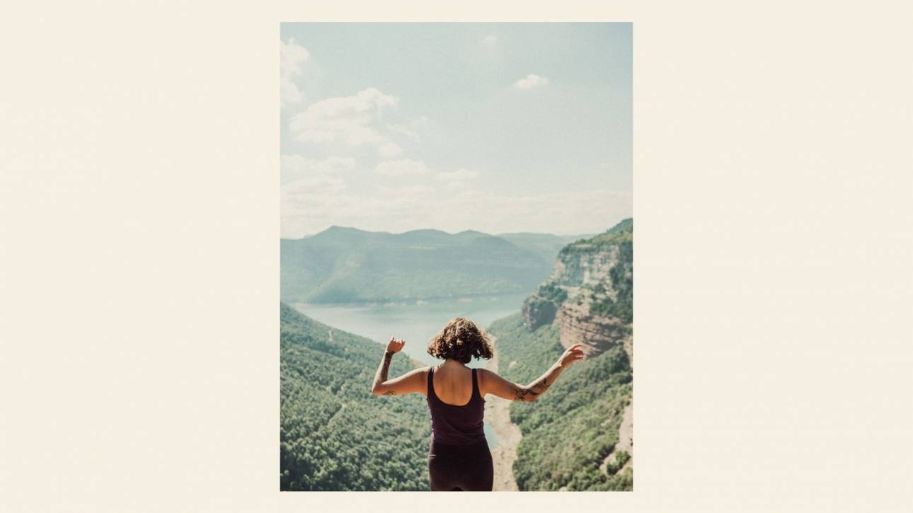 woman viewed from behind with arms open in a summer landscape, illustrating a post about body connection and the body's wisdom