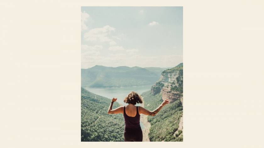 woman viewed from behind with arms open in a summer landscape, illustrating a post about body connection and the body's wisdom