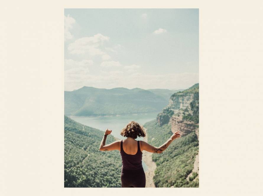 woman viewed from behind with arms open in a summer landscape, illustrating a post about body connection and the body's wisdom