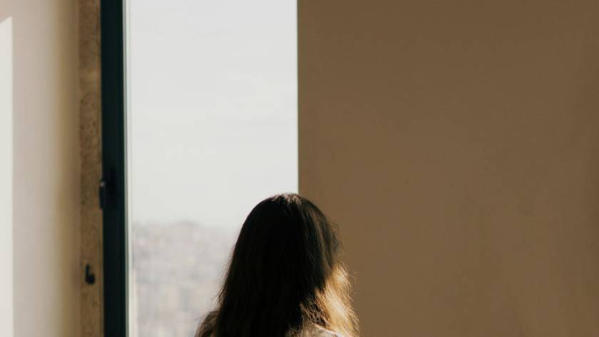 A figure standing small within a large architectural space by an arched window in warm light, illustrating a post about the shy child and self-perception