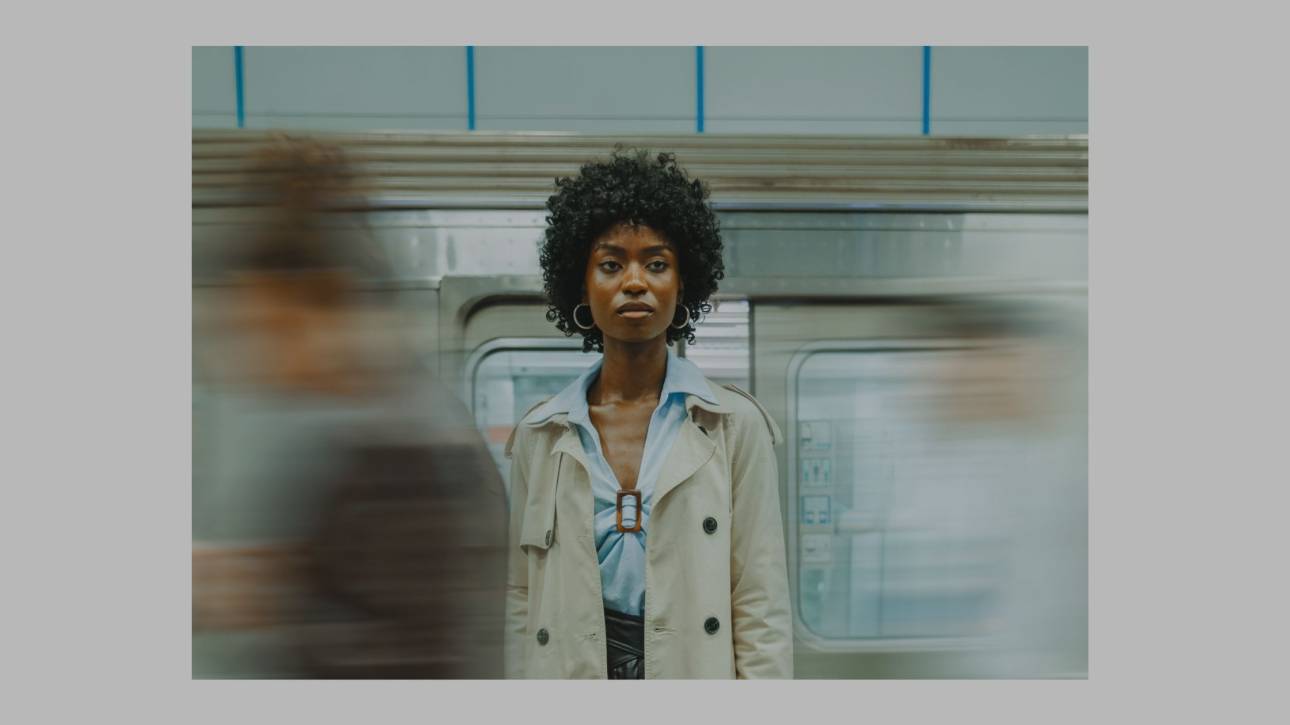 Woman standing composed on a train platform, motion blurred around her, embodying stillness amid surrounding movement
