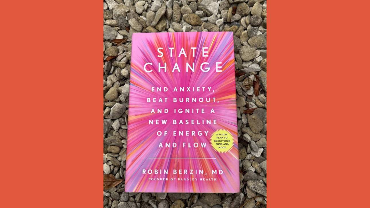 Copy of State Change by Robin Berzin resting on grey gravel, framed by warm orange side panels