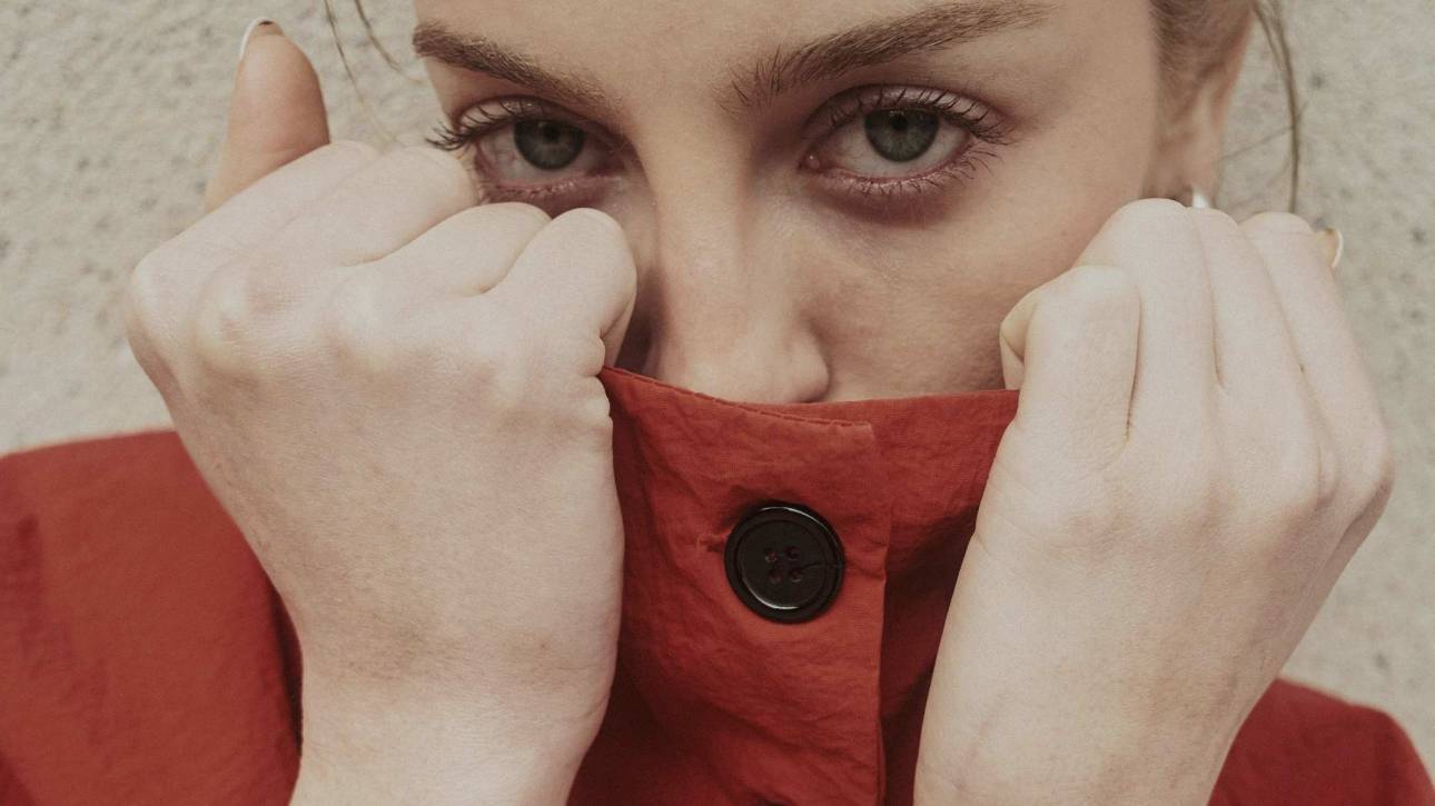 Woman with direct eye contact pulling her collar up to hide her mouth, self-conscious and guarded, illustrating the fear of being judged