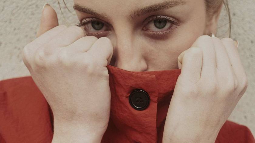 Woman with direct eye contact pulling her collar up to hide her mouth, self-conscious and guarded, illustrating the fear of being judged