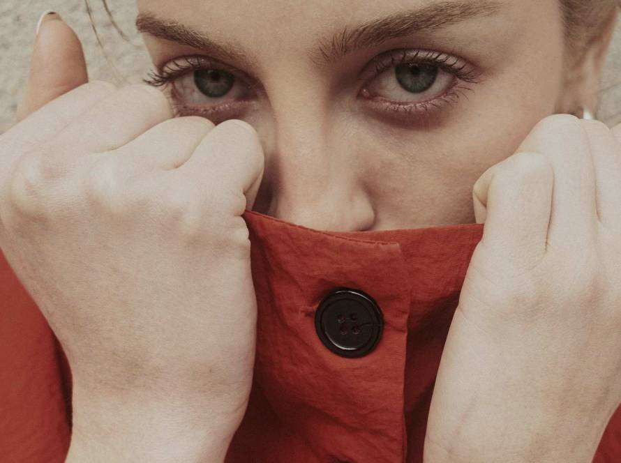 Woman with direct eye contact pulling her collar up to hide her mouth, self-conscious and guarded, illustrating the fear of being judged