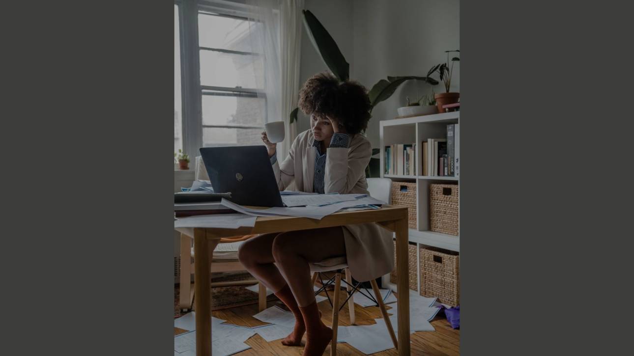 Woman overwhelmed at a paper-strewn desk, head in hand, illustrating the stickiness of procrastination