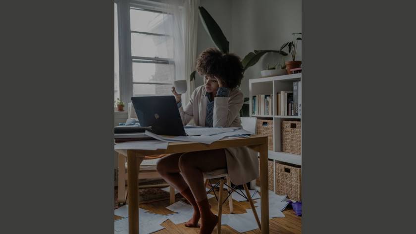 Woman overwhelmed at a paper-strewn desk, head in hand, illustrating the stickiness of procrastination