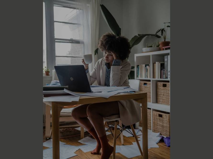 Woman overwhelmed at a paper-strewn desk, head in hand, illustrating the stickiness of procrastination